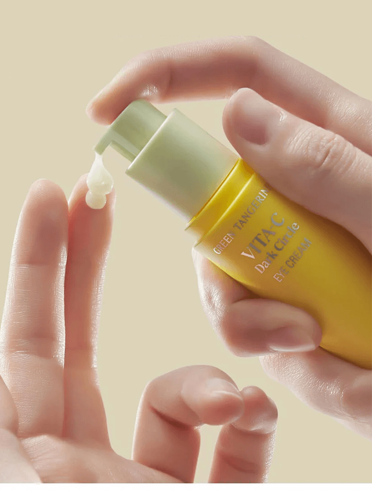 GOODAL Green Tangerine Vita C Dark Spot Care Eye Cream bottle being dispensed gently onto fingers.
