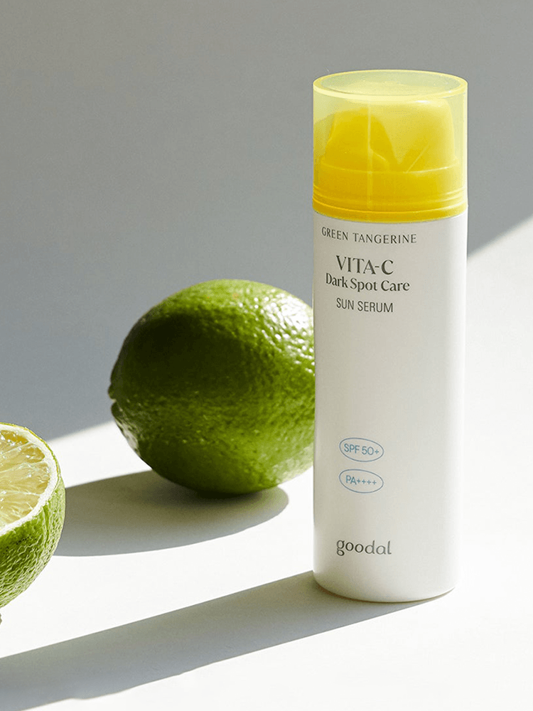 GOODAL Green Tangerine Vita C Dark Spot Care Sun Serum bottle next to fresh limes on a bright background.