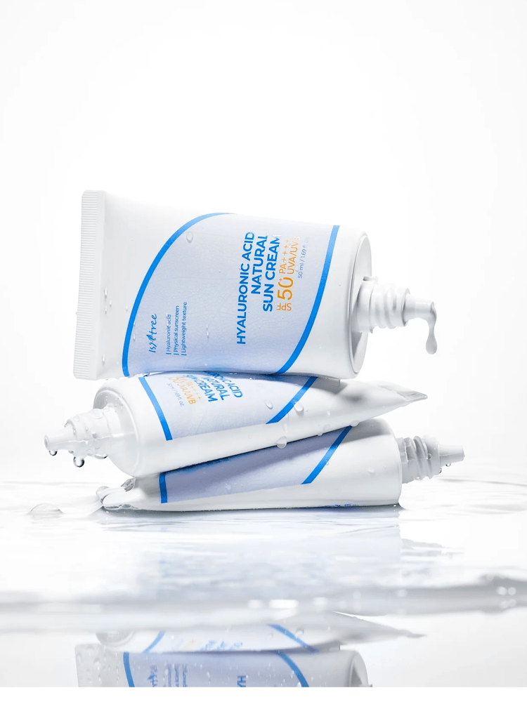 ISNTREE Hyaluronic Acid Natural Sun Cream 50ml tubes stacked on a reflective surface with droplets.