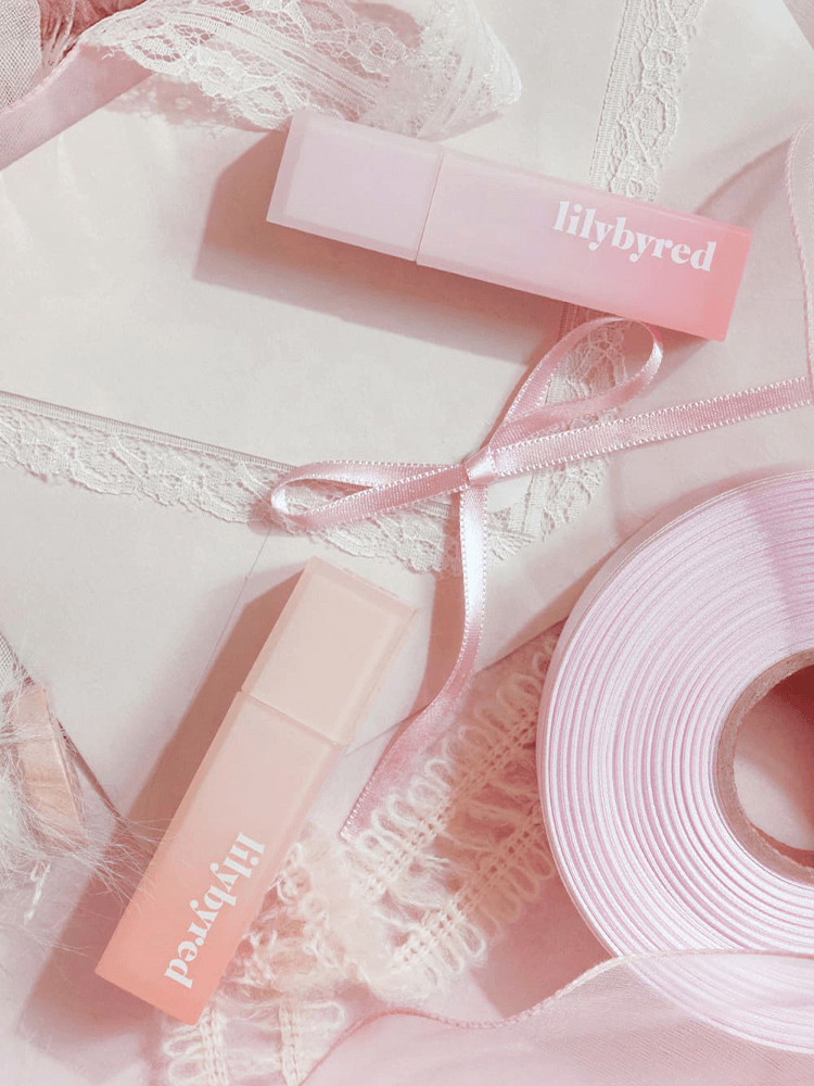 LILYBYRED Sweet Liar Milky Tint in a soft pink packaging, placed on lace and ribbon background.