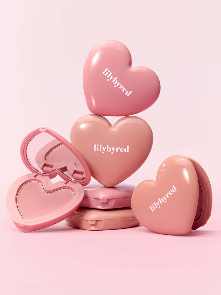 LILYBYRED Luv Beam Cheek Balm heart-shaped packaging in soft pink tones arranged aesthetically on a pastel background.
