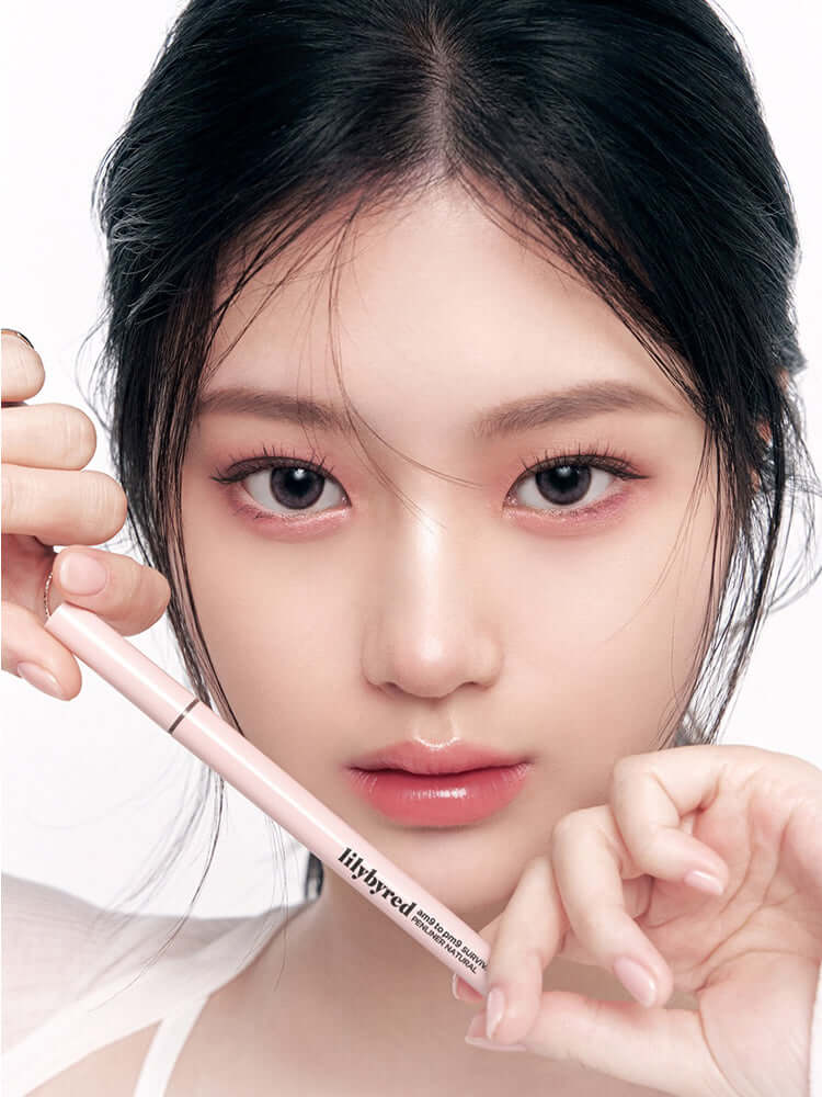 LILYBYRED Am9 To Pm9 Survival Penliner Natural 1g #04 Cherry Brown model holding the pencil with soft natural makeup.