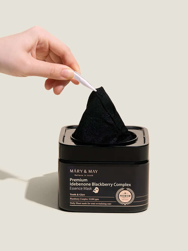 Hand pulling out a sheet from the MARY&MAY Premium Idebenone Blackberry Complex Essence Mask pack.