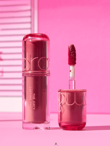 rom&nd The Juicy Lasting Tint Mini 1g bottle and applicator against a pink background.