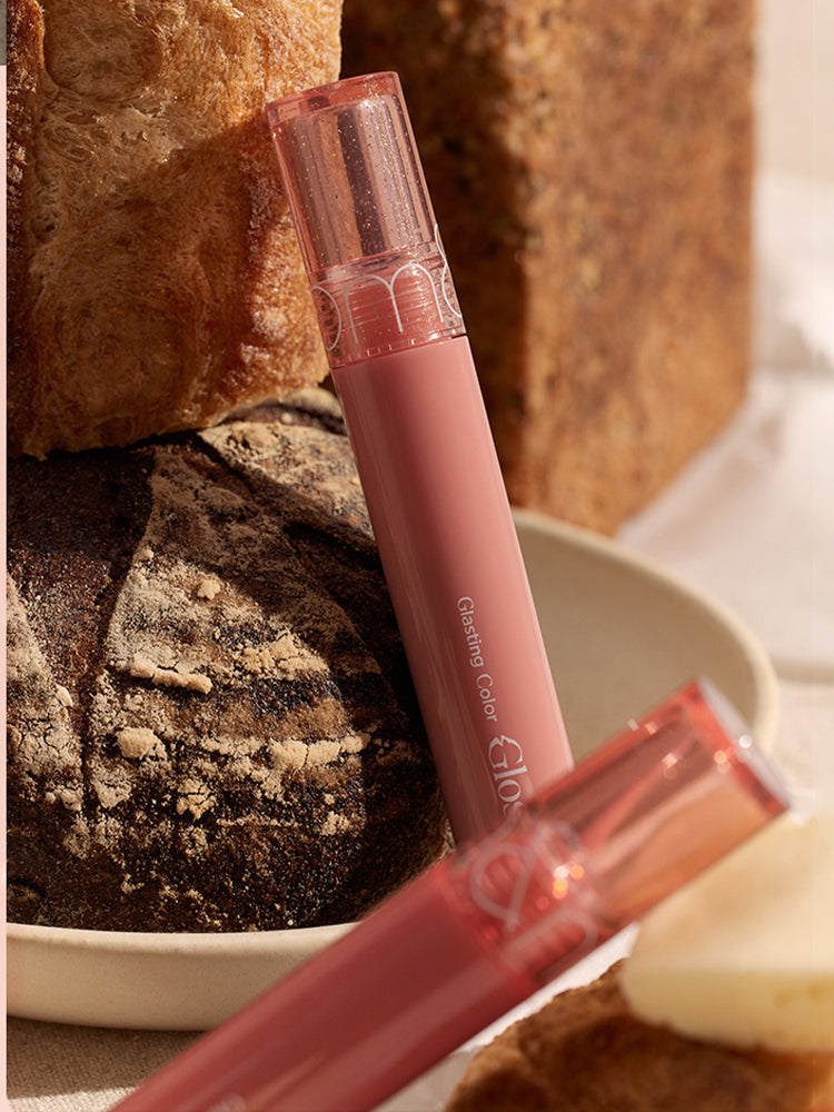 rom&nd Glasting Color Gloss Peach Sparkle displayed with fresh bread highlighting its vibrant color and glossy finish.