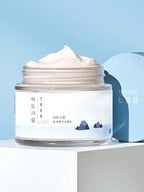 ROUND LAB 1025 Dokdo Light Cream 80ml in a jar against a blue background, showcasing its rich texture.