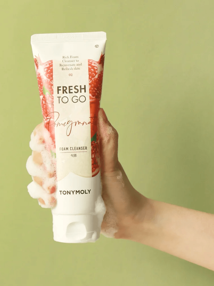 TONY MOLY Fresh To Go Foam Cleanser in hand with foam on a green background, highlighting Pomegranate variant.