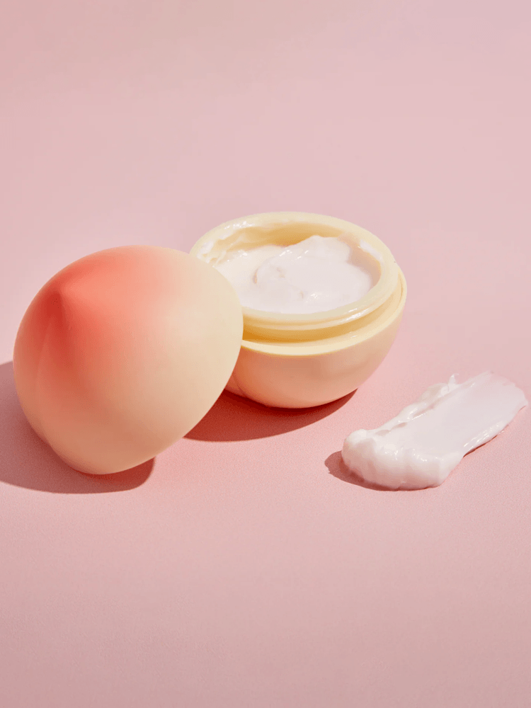 TONY MOLY Peach Hand Cream in peach-shaped container with cream texture against a pink background.